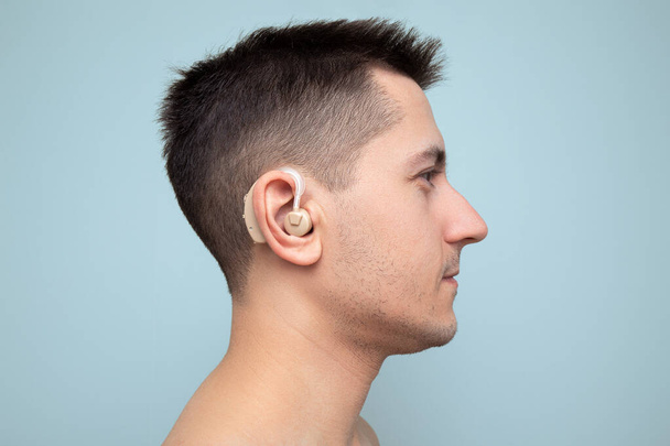 Young man with medical problems with his ears wears a hearing aid to amplify sound. Health and disease treatment concept - Fotó, kép