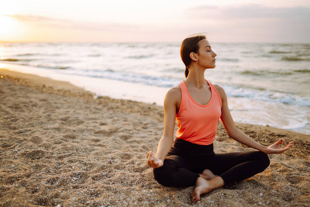 Beautiful woman doing yoga near the ocean barefoot. Young woman in sportswear doing fitness exercise on the beach. Calmness and balance, a healthy lifestyle. - Zdjęcie, obraz