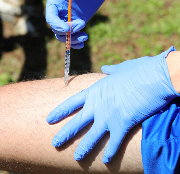 jongen met blauwe latex handschoenen terwijl hij insuline op zijn dij injecteert omdat hij diabetes heeft - Foto, afbeelding