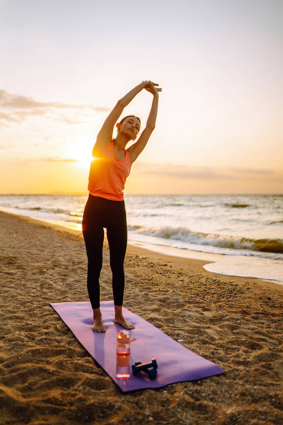 Beautiful woman doing yoga near the ocean barefoot. Young woman in sportswear doing fitness exercise on the beach. Calmness and balance, a healthy lifestyle. - Φωτογραφία, εικόνα