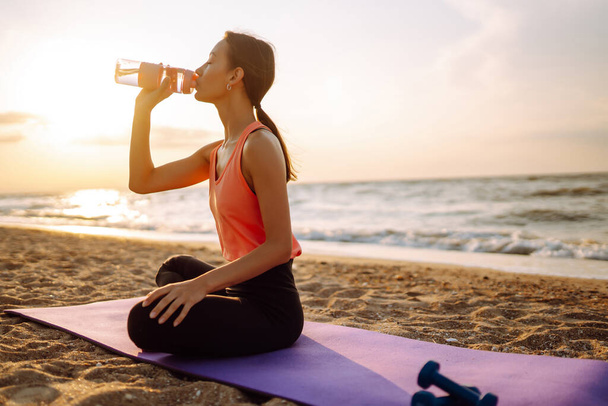 Beautiful woman doing yoga near the ocean barefoot. Young woman in sportswear doing fitness exercise on the beach. Calmness and balance, a healthy lifestyle. - Фото, изображение
