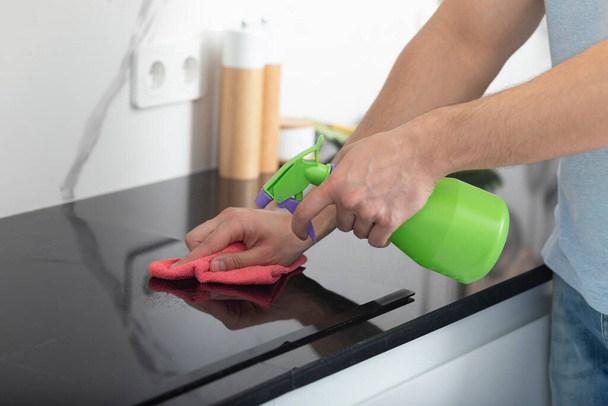 Close up shot of male hands holding bottle spray and cleaning the stove - Photo, image