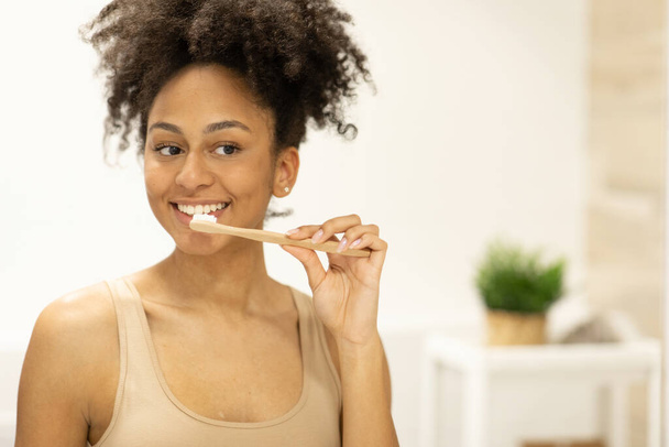 Happy girl looks in the mirror using an ecological toothbrush with whitening toothpaste. High quality photo - Foto, immagini