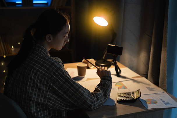 Azjatycka studentka studiuje późno w nocy w domu pod lampą, za pomocą telefonu komórkowego do nauki online, edukacji i koncepcji szkoły - Zdjęcie, obraz