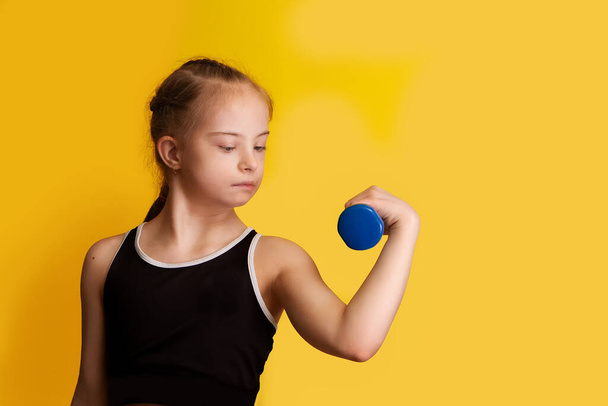 A girl with Downs syndrome goes in for sports, lifting dumbbells with a small weight - Photo, Image
