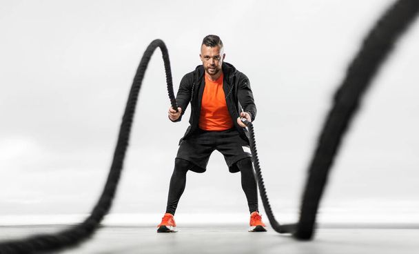 Fat burning battle rope workout. Athletic man with doing sports exercises on the ocean beach. - Zdjęcie, obraz