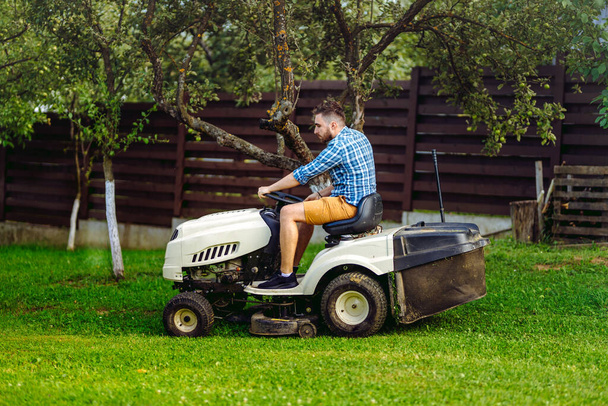 Portrait of gardener using a lawn mowing tractor for cutting grass. professional gardening details - 写真・画像