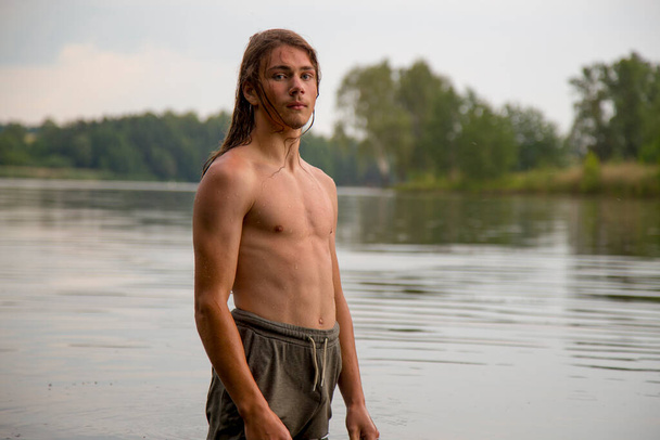 Portrait of a village teenage boy in the river. A long-haired teenager lives harmoniously in nature.  - Photo, image