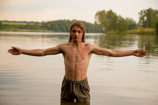 Portrait of a village teenage boy in the river. A long-haired teenager lives harmoniously in nature.  - Zdjęcie, obraz