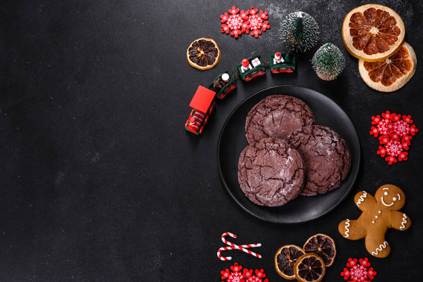 Pyszne świeże herbatniki czekoladowe na ciemnym betonowym tle z zabawkami świątecznymi, suszonymi cytrusami i zabawkami choinkowymi. Przygotowanie świątecznego stołu - Zdjęcie, obraz