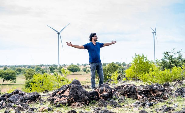 man feeling nature fresh air by stretching arms at wind turbine near - concept of sustainable lifestyle, freedom and relaxation. - Photo, Image