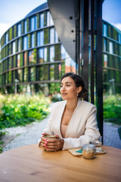 Молода бізнес-жінка тримає і п'є каву в кафе на вулиці в місті. Портрет прекрасної працівниці, яка чекає на клієнта на вулиці Праги. Фотографія високої якості - Фото, зображення