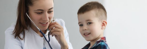 Врач-педиатр слушает сердце стетоскопом маленькому мальчику в клинике. Диагностика заболеваний сердца и легких у детей - Фото, изображение