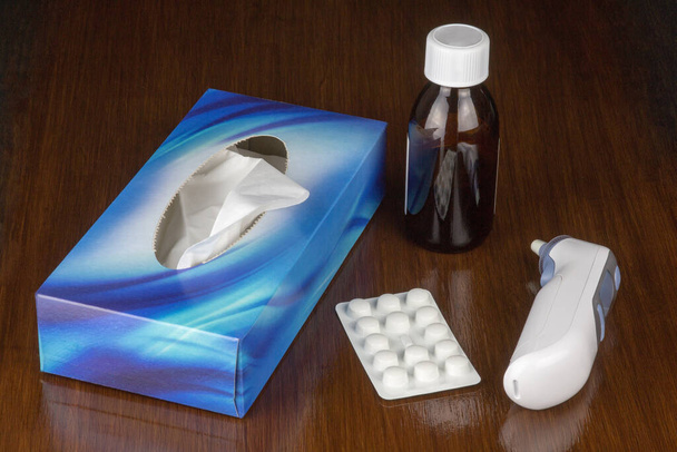 Flacon de médicament avec boîte de thermomètre à tissus et comprimés sur une surface de table polie - Photo, image