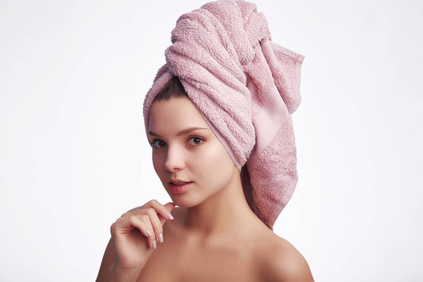 Νεαρή ελκυστική γυναίκα με πετσέτα στο κεφάλι κοιτάζει την κάμερα και χαμογελά σε λευκό φόντο με αντίγραφο χώρο για κείμενο. Φροντίδα προσώπου και έννοια των μαλλιών - Φωτογραφία, εικόνα