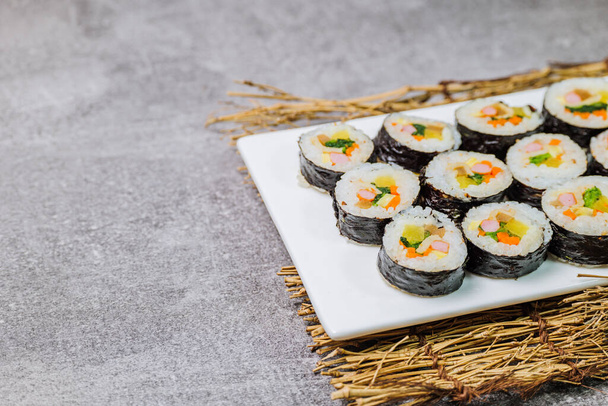 Rice seasoned with salt and sesame oil and rolled up in a sheet of roasted gim (dried laver) with spinach, carrots, and pickled white radish. The long roll is sliced and served in bite-sized pieces - 写真・画像