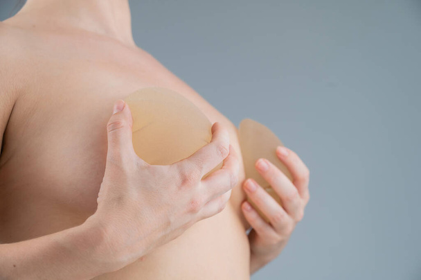 Caucasian naked woman trying on silicone breast implants on a white background - Photo, image