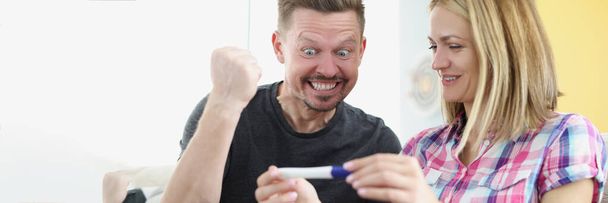 Portrait of happy husband got news about wifes pregnancy, waiting for baby, cheerful man show yes gesture. Woman holding positive pregnancy test. Family growing, happiness concept - Photo, Image