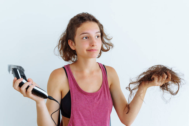 girl shaves long hair baldly with shaving machine. Teenage depression, protest, illness, chemotherapy, attracting attention. teenager looks at clipper in amazement, shaving hair on head - Photo, Image
