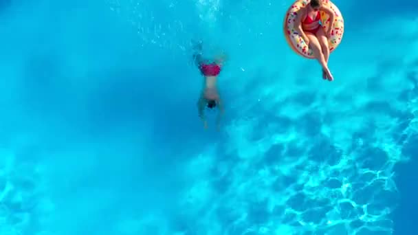 Top down zicht van de man duikt in het zwembad en zwemt terwijl het meisje ligt op een donut zwembad drijven - Video