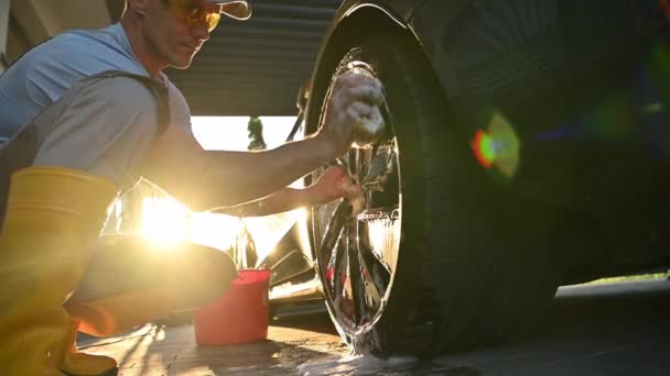 Homens caucasianos limpando rodas de liga de carro moderno em sua garagem usando detergente especial e esponja macia. Tema de manutenção automotiva - Filmagem, Vídeo