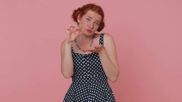 Need some more please give me. Woman showing a little bit gesture with sceptic smile, showing minimum sign, measuring small size asking for help. Ginger girl isolated alone on pink studio background - Footage, Video