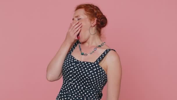 Tired young redhead woman in dress yawning, sleepy inattentive feeling somnolent lazy bored gaping suffering from lack of sleep. Ginger girl with freckles isolated alone on pink studio background - Video