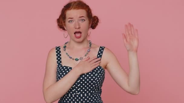 I swear to be honest. Sincere responsible redhead woman raising hand to take oath, promising to be honest and to tell truth keeping hand on chest. Ginger girl with freckles isolated on pink background - Záběry, video