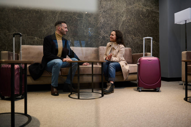 Супружеская пара с чемоданами, коллегами, командой, партнерами в командировке обсуждают планы и проекты в VIP зале для совещаний в ожидании рейса в терминале вылета аэропорта - Фото, изображение