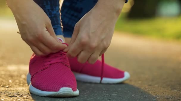 Vrouw veters strikken tijdens het joggen of lopen bij zonsondergang, close-up. Langzame beweging - Video
