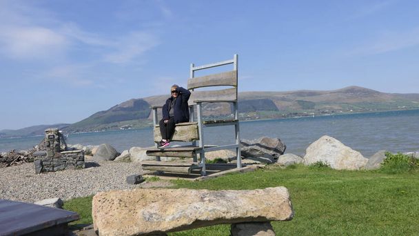 Женщина, сидящая на очень большом стуле у моря - Фото, изображение