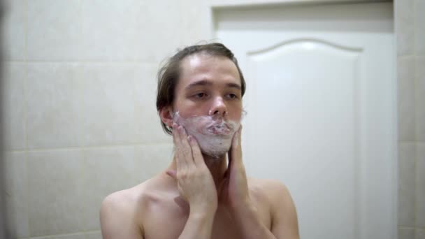 Guy legt Rasierschaum auf sein Gesicht und seinen Hals. Den Bart rasieren. - Filmmaterial, Video