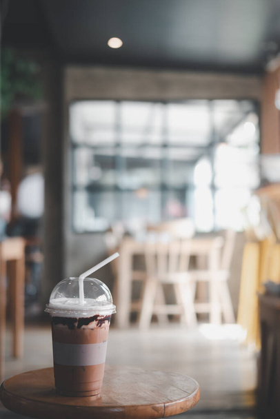 Kahve dükkanının ahşap masasında plastik bardakta buzlu kahve. Tazeleyici içecek. - Fotoğraf, Görsel