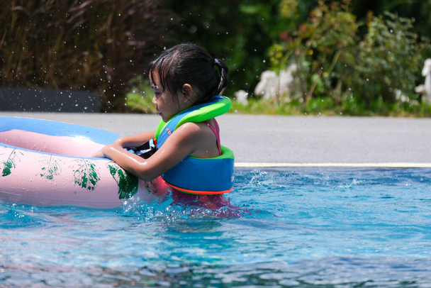 Alle bambine piace nuotare in piscina. Carino ragazza asiatica che indossa un giubbotto di salvataggio si sta divertendo a giocare nella piscina all'aperto. Attività estive salutari per bambini. - Foto, immagini