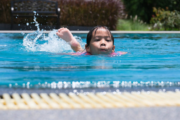A kislányok szeretnek úszni a medencében. Aranyos ázsiai lány, mentőmellényt visel, és jól érzi magát a kinti medencében. Egészséges nyári tevékenységek gyerekeknek. - Fotó, kép