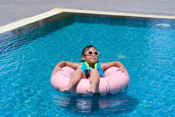 Маленька дівчинка в купальнику розслабляється на надувному кільці в басейні. Мила дівчинка грає в басейні в сонячний день. Концепція літнього способу життя
. - Фото, зображення