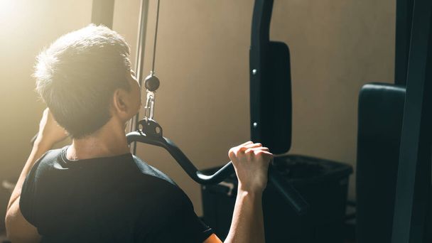 Hombre haciendo ejercicio en la máquina de cable, el fortalecimiento del cuerpo en el gimnasio, vista trasera. - Foto, Imagen