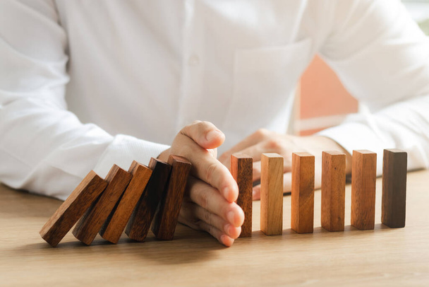 Risk management, business man hand Stop the continuous falling of wooden dominoes, stop the impact of the business crisis. hedging Solving business problems for success. - 写真・画像
