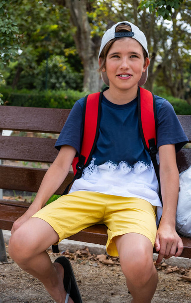Mignon garçon souriant dans un chapeau regardant la caméra. Repos sur un banc par une chaude journée d'été - Photo, image