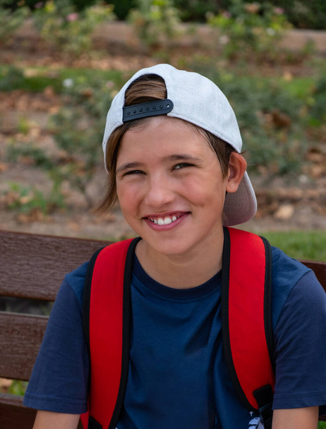 Cute smiling boy in a hat looking at the camera. Resting on a bench on a hot summer day - 写真・画像