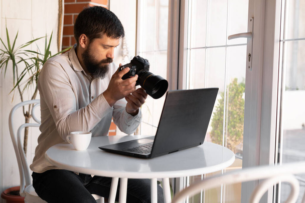 Creative Photographer working with laptop and digital camera at cafe. Professional journalist or freelancer looking at photographs with DSLR camera, close up - Fotografie, Obrázek
