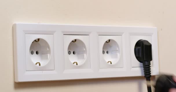 Man voegt stekker van huishoudelijke apparaat in witte socket geïnstalleerd in beige muur. Huishouder schakelt elektronisch apparaat thuis in close-up - Video