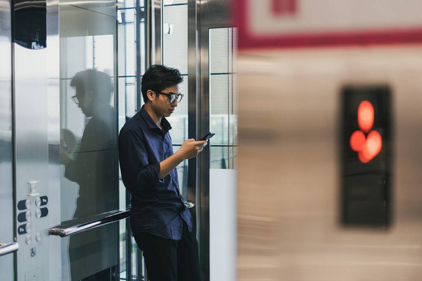 Egy fiatal ázsiai férfi kezei, okos mobiltelefonnal a liftben. - Fotó, kép
