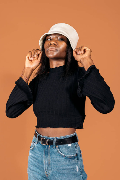 Stock photo of cool black girl wearing hat posing in studio shot against brown background. - Fotó, kép
