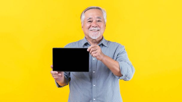 Азиатский пожилой человек, старик показывает смартфон, планшетный компьютер с пустым экраном, черный экран, пустое место для копирования рекламного баннера изолированы на желтом фоне, Mock Up Image - Фото, изображение