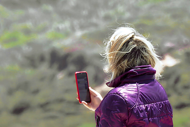 Woman in purple jacket taking pictures with mobile phone - Foto, Imagen