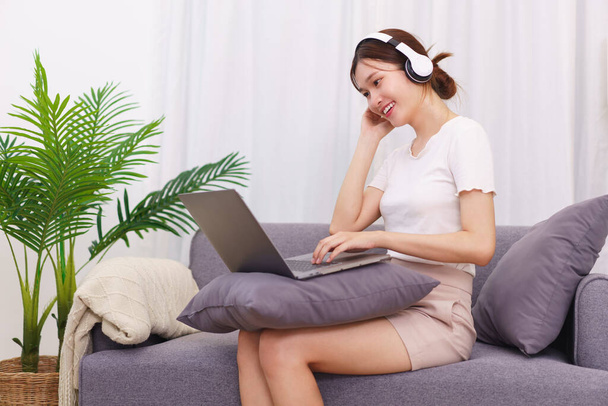 Estilo de vida en concepto de sala de estar, Mujer asiática joven en auriculares para escuchar música en el ordenador portátil. - Foto, imagen