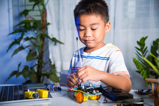 Asian kid boy plugging energy and signal cable to sensor chip with Arduino robot car, Little child remotely learn online with car toy, STEAM education AI technology course school learning lesson - Foto, imagen