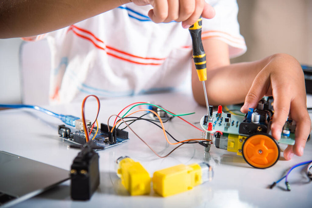 Little child tighten the nut with a screwdriver to assemble car toy, Asian kid boy assembling the Arduino robot car homework project at home, education AI technology workshop school learning lesson - 写真・画像