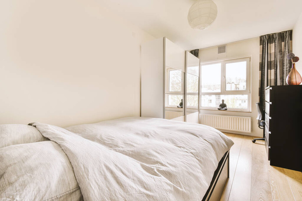Komfortní postel se nachází v blízkosti zářící v moderní ložnici s malým okénkem - Fotografie, Obrázek